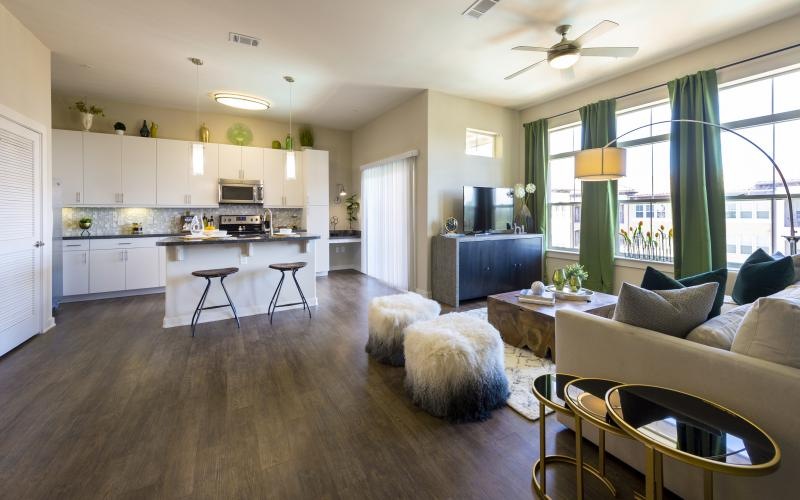 a living room with large windows leading into a kitchen